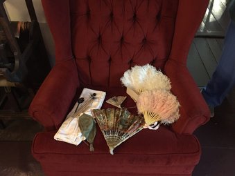 A photo of a red armchair with a flower bouquet, a handkerchief, and a fan on it.